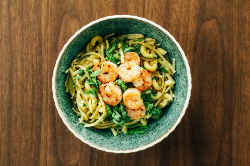 A bowl of noodles with spinach and shrimp on a wood table